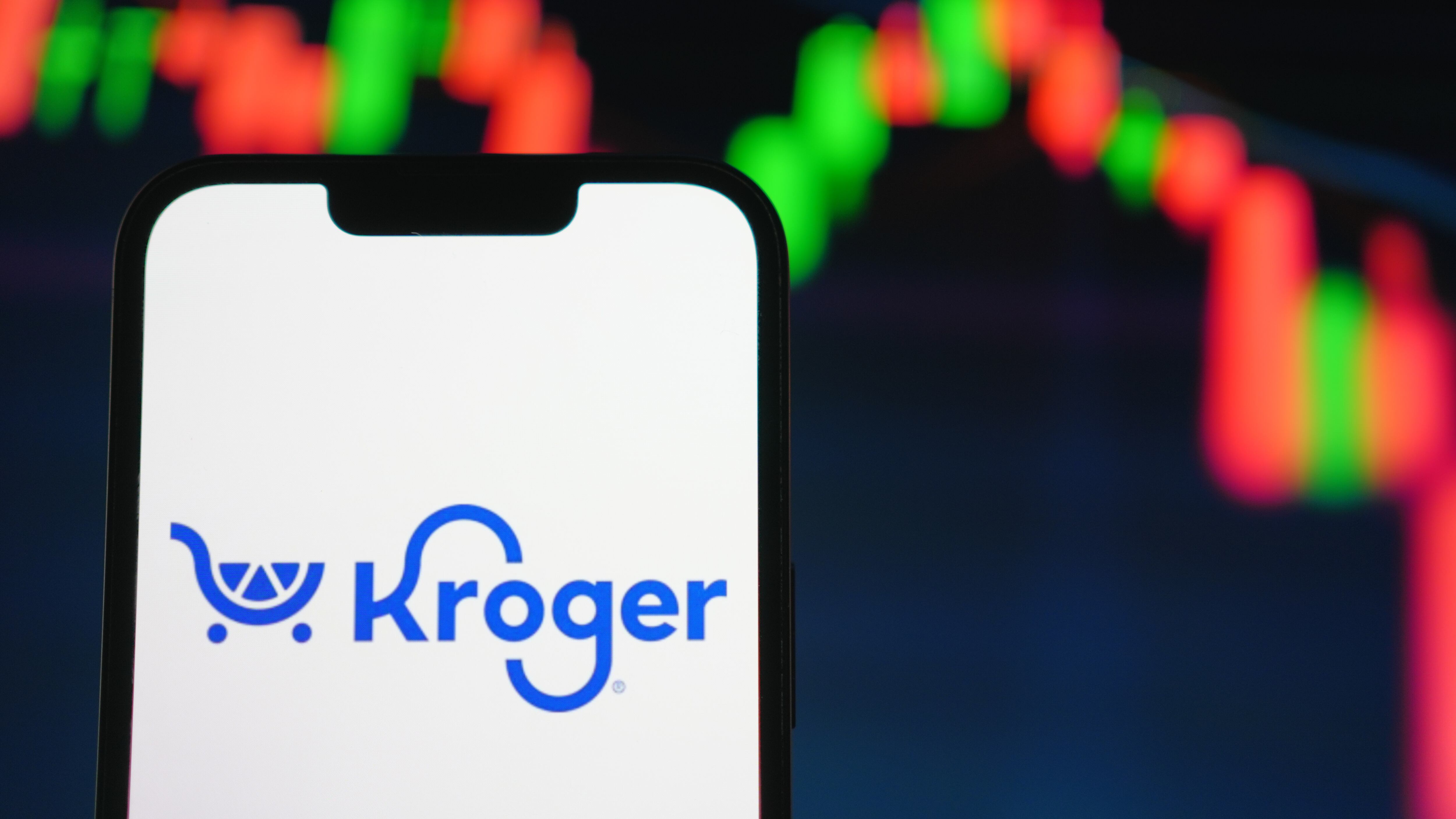 A mobile phone displaying the company logo of Kroger, with a stock chart in the background.